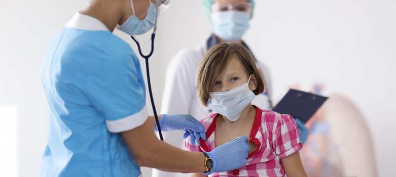 Portrait of girl being examined by pediatrician doctor with stethoscope tool. Calm little girl sit in office and get checkup. Medicine, appointment concept