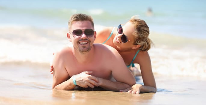 Portrait of cheerful couple resting together on beach laying on coastline and posing. Middle aged man and pretty woman in sunglasses. Beach, summer concept