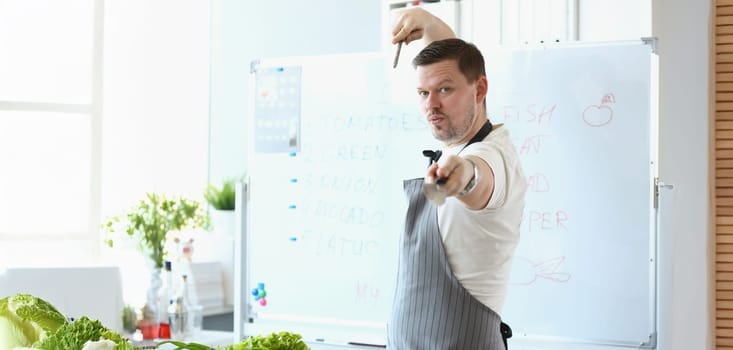 Portrait of attractive male chef standing in apron and pretend hes fighter with cooking knife. Blogger chef discover healthy eating habits. Food concept