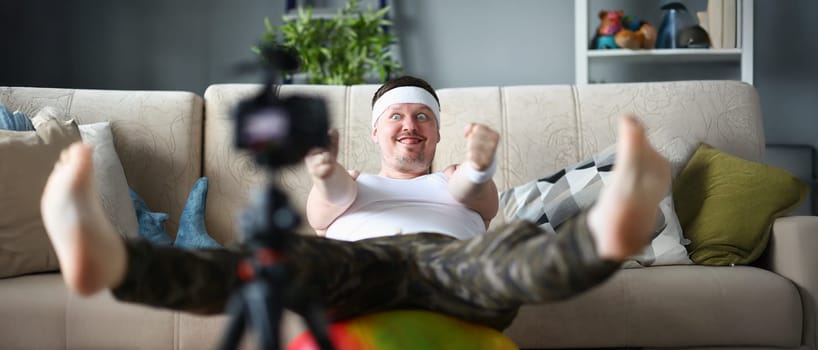 Portrait of man in sportswear perform exercise on ball with funny facial expression. Active person start channel on social media. Internet, sport concept