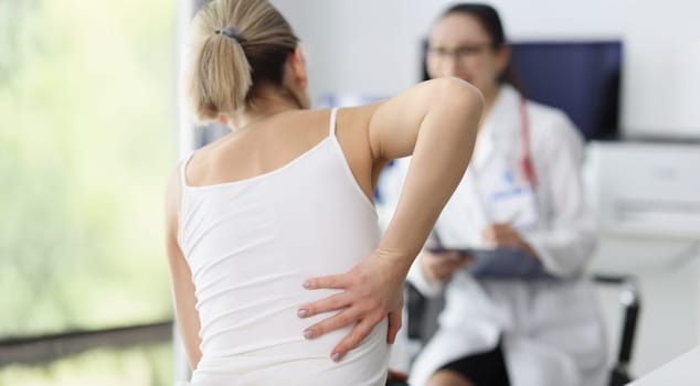 Close-up of female patient complain on back pain and touch side of body. Doctor listen to client and propose diagnostic. Healthcare, trauma surgeon concept