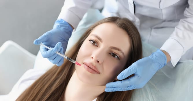 Portrait of young woman gets injection of botox in her lips, cosmetologist using syringe. Cosmetology, beauty treatment, plastic surgery, clinic concept