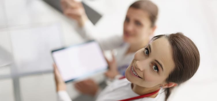 Top view of women working in hospital spend pause with tablet device. Smiling nurse hold gadget with white screen. Pause from work, pastime, clinic concept