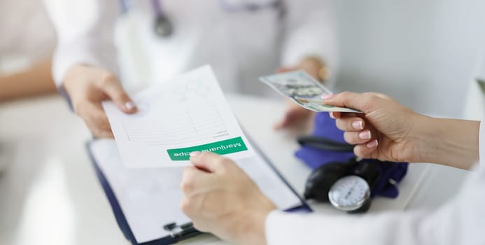 Close-up of patient give banknote money to doctor for marijuana recipe in hospital. Paper with hemp prescription. Alternative medicine, treatment concept