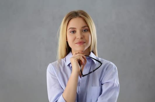 Portrait of attractive young woman posing in strict outfit hold black glasses. Blonde successful female confident model. Modeling, psychologist concept