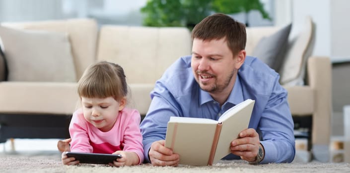 Portrait of father reading book to daughter while child stare at smartphone. Quality time with kid on holiday. Childhood, parenthood, addiction concept