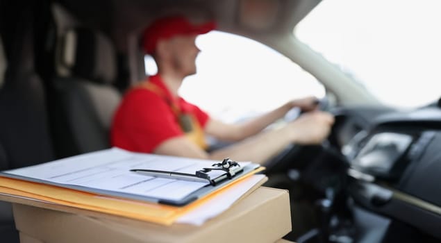 Close-up of docs on box and smiling courier deliver packages to people on car. Worker in special red uniform. Delivery service, shipping, transfer concept