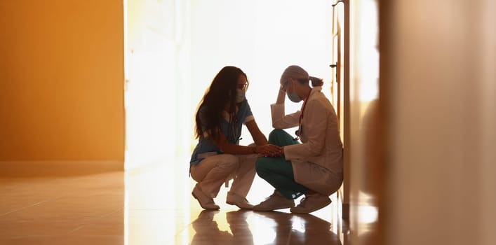 Low angle of tired medical worker after hard long surgery sitting on floor. Nurse support colleague doctor. Medicine, save life, health, tragedy concept