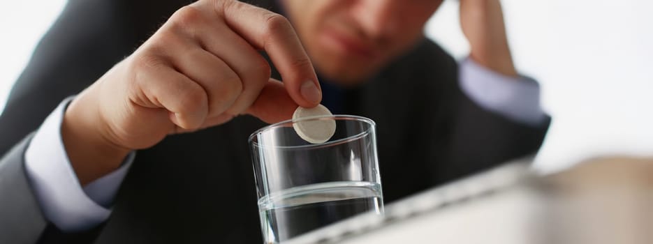 Close-up of tired man put tablet in glass with water to stop headache because of big workload. Aspirin medication to relief pain. Medicine, remedy concept