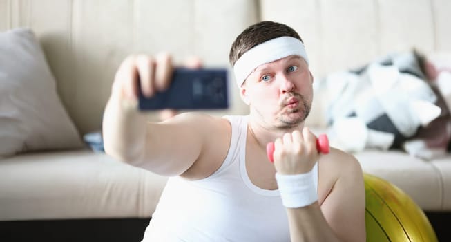 Portrait of sportsman training at home lifting dumbbell and take selfie for social media channel. Middle aged blogger create sport content. Hobby concept