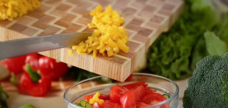 Close-up of professional chef put in glass bowl cutted pieces of yellow pepper add to fresh tomatoes. Person follow delicious new recipe. Cooking concept