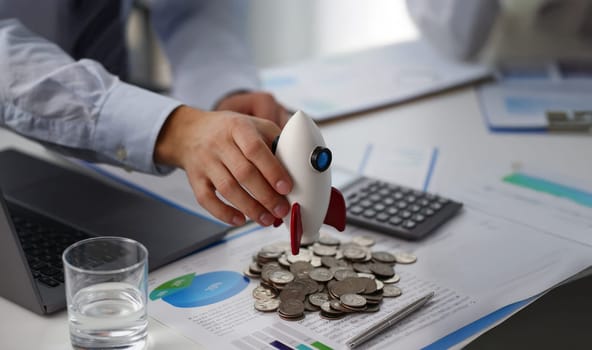 Close-up of person hold rocket model over bunch of coins and business papers on table. Launch rocket, startup, open business, risk and strategy concept