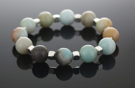 Close-up of shiny cute hand bracelet made of semiprecious stones. Real energy crystal presented on grey background with reflection. Heal, accessory concept