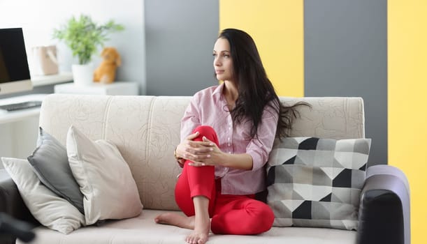 Portrait of brunette pensive young woman looking away sitting on couch at home. Female dreaming about holiday, make plans in mind. Interior, rest concept