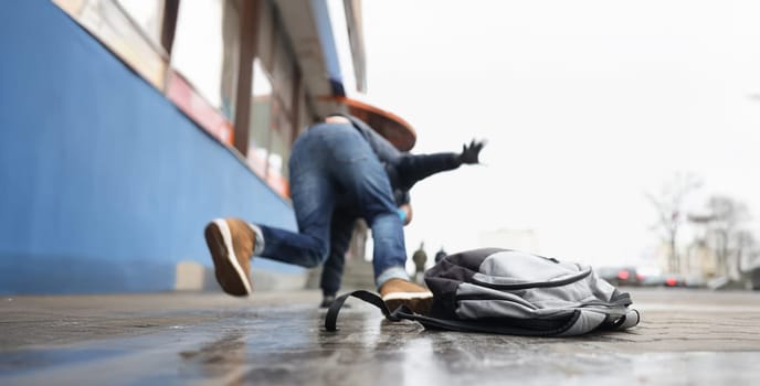 Close-up of person get injury after falling on slippery ground in winter season. Personal backpack lay on asphalt ice. Accident, trauma, clumsy concept
