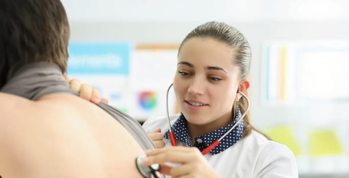 Portrait of young female doctor listen to patients back with stethoscope equipment. Concentrated medical worker examine body, diagnostic. Medicine concept