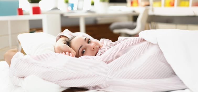 Portrait of happy young woman waking up in cozy home bed in good mood. Lovely female in pyjamas stretching after waking up. Good morning, awake concept