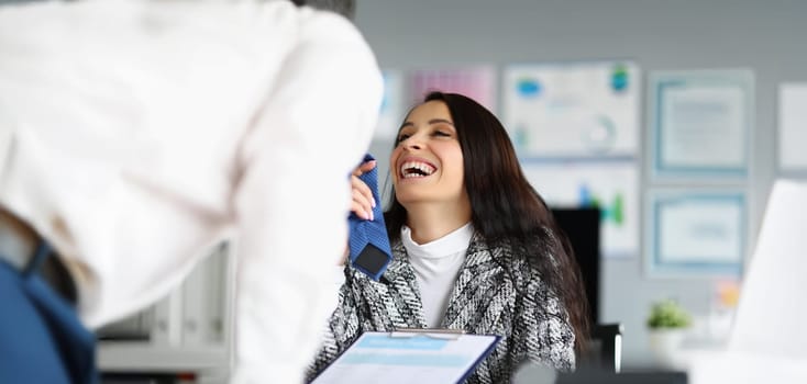 Portrait of businesswoman flirting with corporate male worker touching his tie and laughing. Female boss start relationship at work. Office romance concept