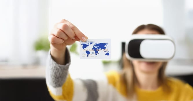 Close-up of young woman wearing virtual glasses and showing credit card. Payment via internet banking for participating in online game. Technology concept