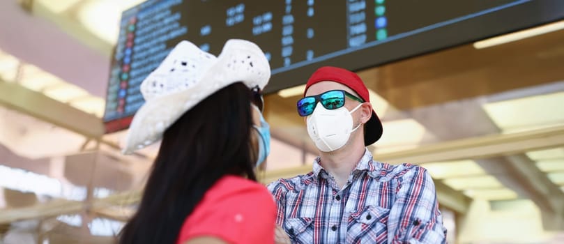 Portrait of couple going on vacation during pandemic wait for their flight in airport. Man and woman wear protective face masks. Virus, holiday concept