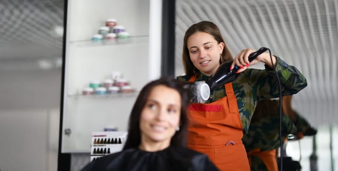 Portrait of smiling hairdresser using hairdryer for treatment with hair and being creative. Professional equipment for work with hair. Wellness concept