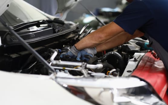 Close-up of professional mechanic male repair detail in automobile on pit station. Qualified garage worker in uniform fix car. Maintenance service concept