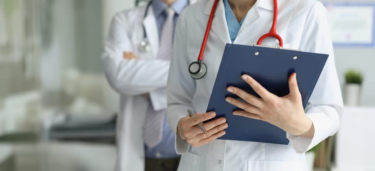 Close-up of medical coworkers in uniform posing in clinic with prescription paper. Professional hospital workers examine patients history. Medicine concept