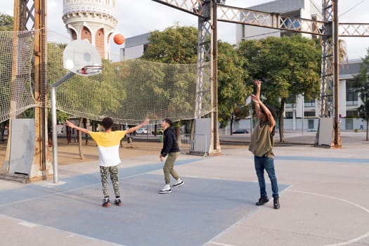 three focused multiethnic teen friends having fun playing basketball on sports ground in city park, concept of youth and urban lifestyle