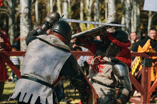Festival of historical clubs in the Park. Reconstruction of medieval battles. Two knights with shields fight with swords in the arena. Bishkek, Kyrgyzstan - October 13, 2019