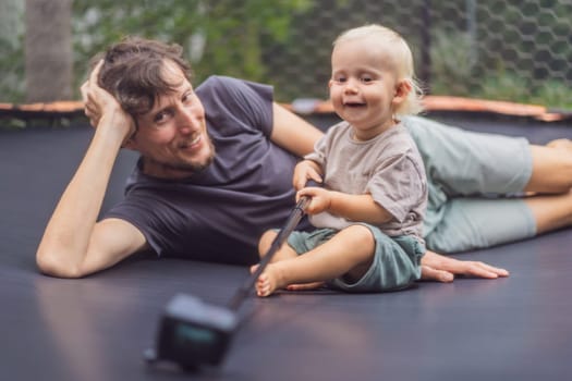 Dad and toddler sitting on an outdoor trampoline with an action camera. Family bonding, playful moments, and outdoor fun concept.