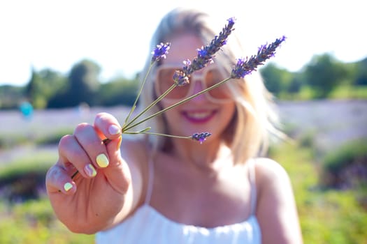 A smiling young woman holds a lavender flower in her hand, looking at the camera. Her joyful expression and delicate flower create a serene and uplifting moment.