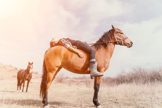 A woman lays across the back of a brown horse with her legs dangling. Two other horses are in the background.