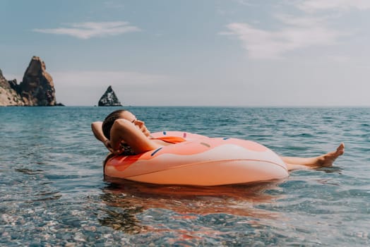 A woman floats on a pink flamingo pool float in the ocean, looking out at a rocky headland in the distance.