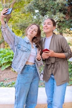 Two young caucasian women taking a selfie with smartphone outdoors