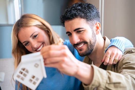 Couple is holding a small model house, symbolizing the joy of buying a new home. They are sitting close together, sharing a moment of happiness and excitement as they look at the miniature house.