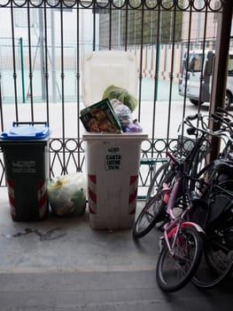 Cremona, Italy August 31st 2024 Overflowing public trash bins standing beside bikes parked on the street on a cloudy day