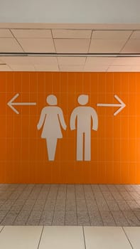 Wall with large male and female signs and directional arrows on orange wall at entrance to restroom. Direction to toilet with gender separation in restroom