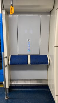Vertical photo of special standing area in underground train with ledge to lean on wall next to USB charging ports for phone, convenience in public transport metro