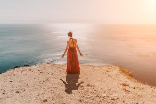 Woman red dress sea. Female dancer in a long red dress posing on a beach with rocks on sunny day. Girl on the nature on blue sky background