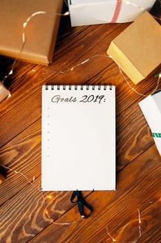 Prepare for Christmas with Notepad and gifts. Notebook with the words Goals 2019 lies on a wooden table.