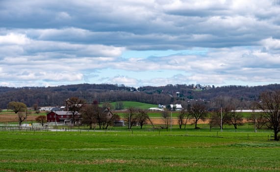 The view reveals a serene countryside with several farms nestled among rolling green hills, framed by a cloudy sky that hints at a changing season.