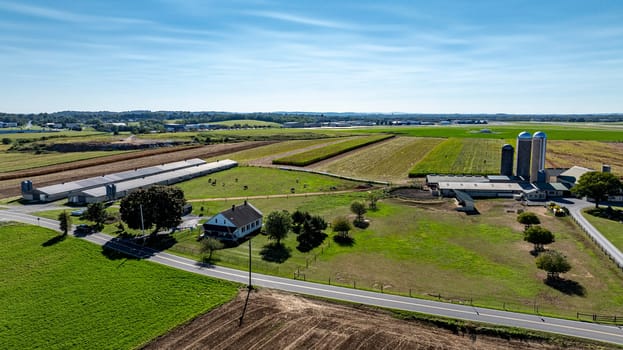 A vast expanse of farmland under a clear blue sky features silos and a quaint rural house. Lush fields stretch into the distance, showcasing the beauty of agricultural life.