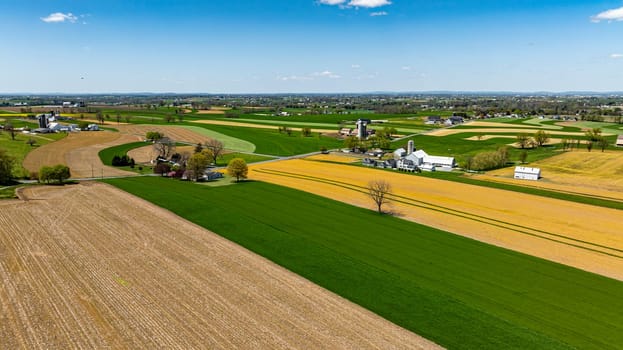 A sweeping view of lush green and golden fields stretches across the landscape, featuring farm buildings and trees, all bathed in bright sunlight on a clear day.