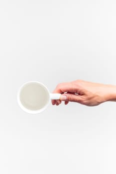 An empty white ceramic cup in a female hand on a white background, banner food mockup, top view
