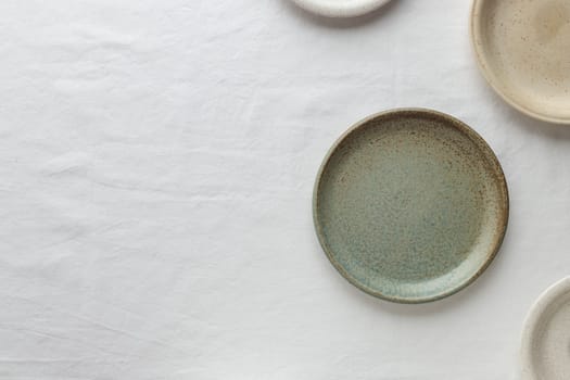 Empty rustic vintage plates dinnerware on a white tablecloth with copy space as a background for meal food dishes, food mock-up