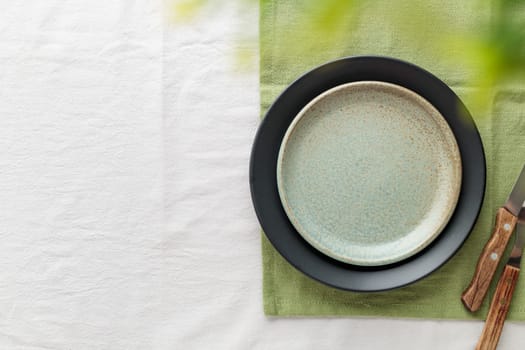 Empty vintage green plate on a white tablecloth with cutlery, copy space as a background for meal dishes, food mock-up