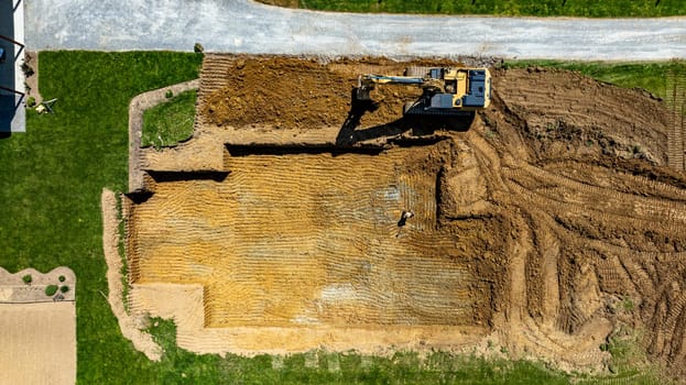 An excavator is digging into the ground to prepare a foundation for building a new structure in a residential neighborhood. The area is clear, showcasing the construction site layout.