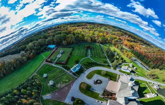 The scene captures a stunning aerial perspective of a landscape in autumn, showcasing colorful foliage, neatly arranged gardens, and clear blue skies. The vibrant trees create a picturesque backdrop.