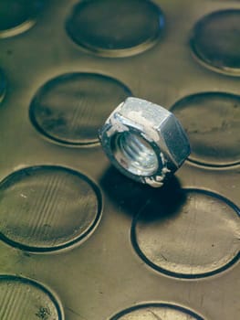 Lone metal nut sits on a dark, textured surface, possibly in a workshop or industrial setting. The image evokes a sense of simplicity and functionality