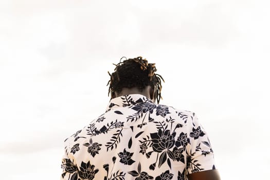 back view of a stylish young black man in a flower shirt with the sky in the background, concept of freedom and lifestyle, copy space for text